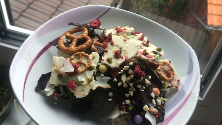 Eine handgef&uuml;llte Sch&uuml;ssel mit Bruchschokolade und weiteren leckeren Zutaten steht vor einem Fenster mit Blick auf Dachziegel.