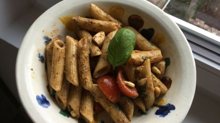 Ein bunter Nudelsalat in einer Sch&uuml;ssel, der auf einem Fensterbrett steht, umgeben von Tageslicht und einem Fensterblick.