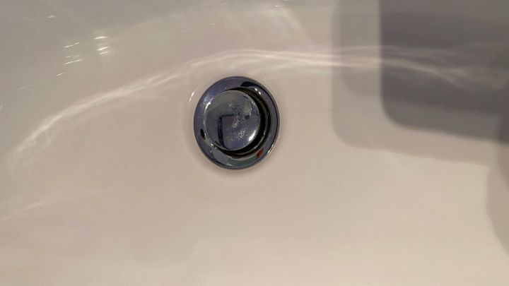 Ein Abflussloch in einer Badewanne zeigt sich in der N&auml;he von glattem, wei&szlig;em Material, das Wasser abf&uuml;hren soll.