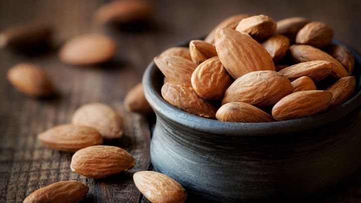 Mandeln liegen in einer kleinen Sch&uuml;ssel und verstreut auf einem rustikalen Holztisch, ideal f&uuml;r laktosefreie Ern&auml;hrung.