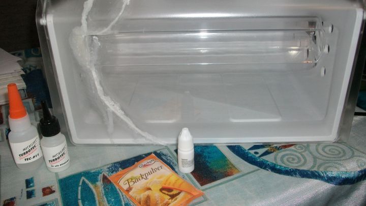 Eine besch&auml;digte Gefrierschublade liegt auf einem Tisch, umgeben von Backpulver und Sekundenkleber f&uuml;r die Reparatur.