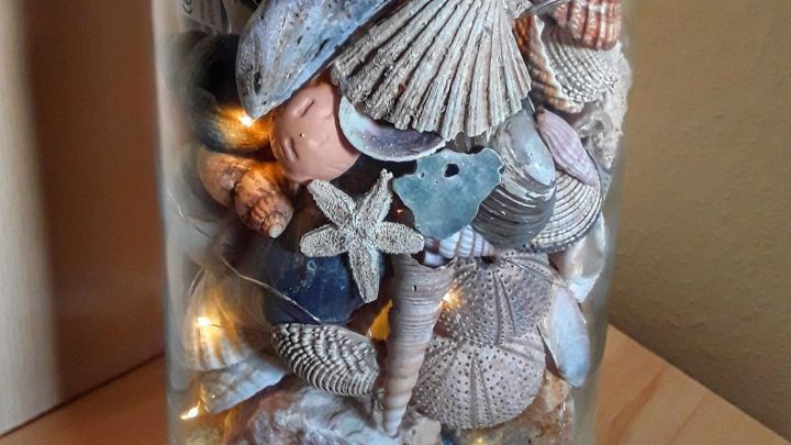 Ein Glasbeh&auml;lter zeigt eine dekorative Anordnung von Muscheln und Sand, die an Urlaubserinnerungen erinnert.