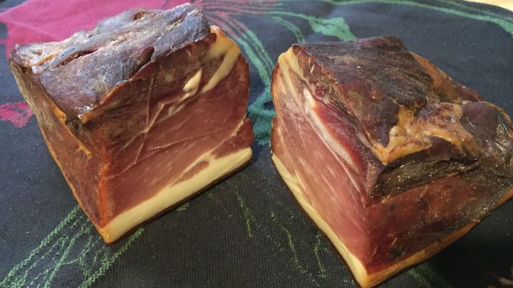 Zwei St&uuml;cke selbst ger&auml;ucherter Schinken liegen auf einem Tisch, umgeben von einer bunten Tischdecke.