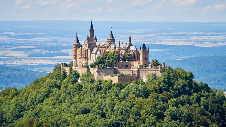 Eine beeindruckende Burg thront auf einem H&uuml;gel in der schw&auml;bischen Alb, umgeben von &uuml;ppigem Gr&uuml;n und unter blauem Himmel.