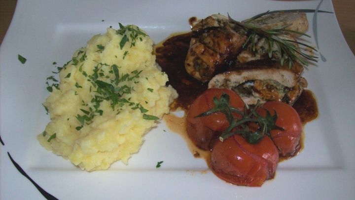 Die Kr&auml;uter-Putenrouladen liegen neben geschmorten Tomaten und cremigem Kartoffelbrei auf dem Teller.