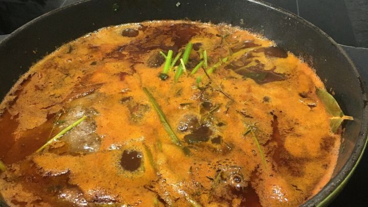 In einem gr&uuml;nen Topf k&ouml;cheln zarte Ochsenb&auml;ckchen in einer aromatischen Rotweinso&szlig;e auf der Herdplatte.