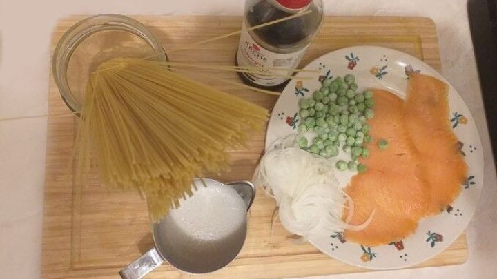 Spaghetti, Lachs und Zutaten liegen auf einem Holzbrett, bereit zur Zubereitung einer sahnigen Pasta-Sauce.