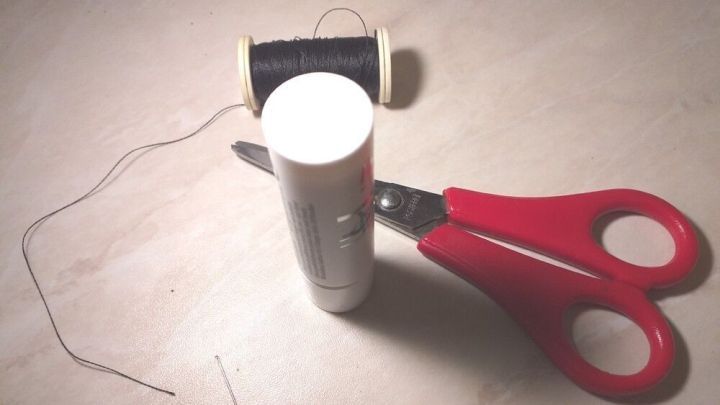 Ein rotes Scherenset liegt neben einer N&auml;hspule und einer Kleberolle auf einem hellen Untergrund, w&auml;hrend der Faden vorbereitet wird.