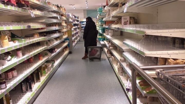 Eine Person mit Einkaufswagen steht in einem leeren Gang eines Supermarkts, w&auml;hrend sie Lebensmittel kauft.