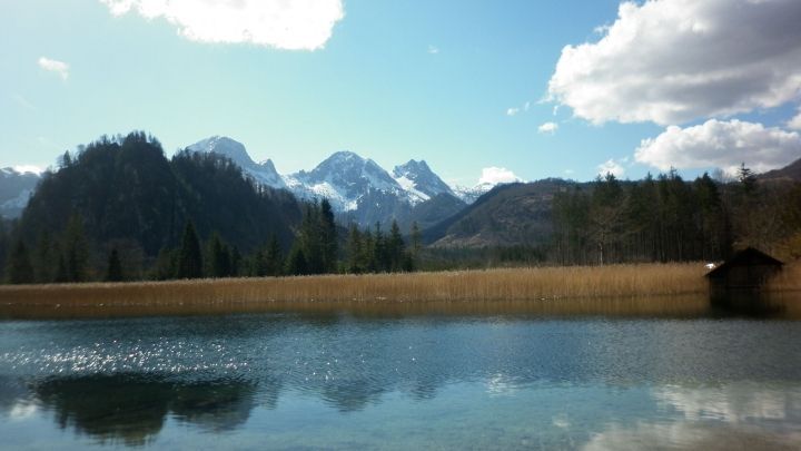 Ein ruhiger See spiegelt die umliegenden Berge und den blauen Himmel wider, umgeben von der friedlichen Natur.