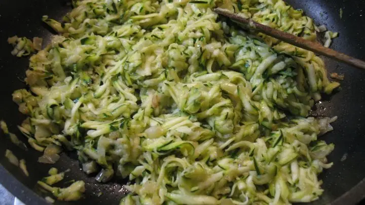 Zucchiniraspel werden mit Zwiebelw&uuml;rfeln und Knoblauch 10 bis 15 Minuten bei m&auml;&szlig;iger Hitze unter st&auml;ndigem R&uuml;hren ged&uuml;nstet, bis die Fl&uuml;ssigkeit verdampft ist, danach l&auml;sst man alles abk&uuml;hlen. 