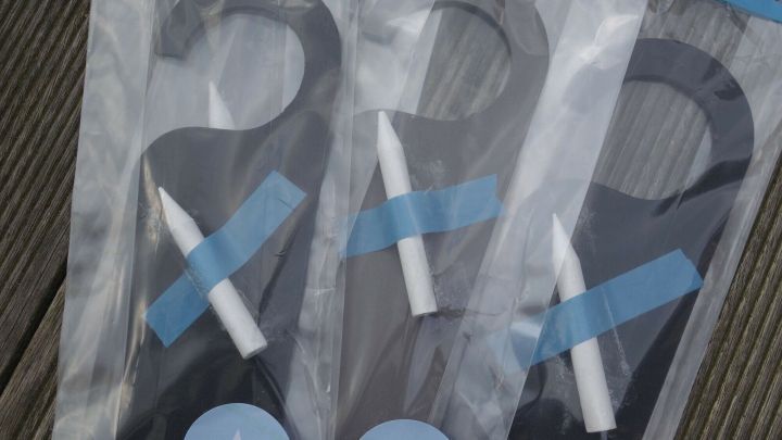 Schlichte T&uuml;ranh&auml;nger aus Karton liegen in durchsichtigen T&uuml;ten auf einem Holzuntergrund und sind als Give-away verpackt.