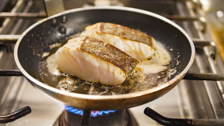 Im Bratpfanne braten zwei Fischfilets in erhitztem &Ouml;l, w&auml;hrend sie auf einem Herd f&uuml;r die Zubereitung vorbereitet werden.