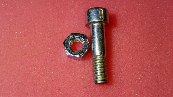 Eine Schraube und eine Mutter liegen auf einem roten Untergrund, bereit zum fachm&auml;nnischen K&uuml;rzen und Befestigen.