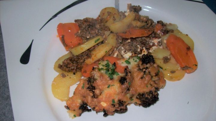 Ein bunter Hack-Auflauf mit M&ouml;hren und Kartoffeln liegt auf einem wei&szlig;en Teller, umgeben von einer eleganten Tischdeko.