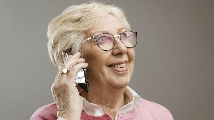 Eine &auml;ltere Frau h&auml;lt ein Handy ans Ohr und l&auml;chelt, w&auml;hrend sie mit ihrem Enkelkind w&auml;hrend der Corona-Krise telefoniert.