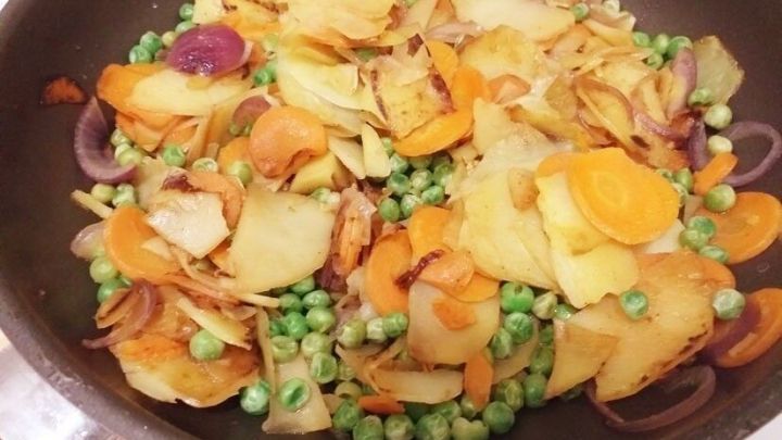 Bunte Gem&uuml;sepfanne brutzelt in einer Pfanne, gef&uuml;llt mit Kartoffeln, Erbsen und Karotten, lecker und s&auml;ttigend.