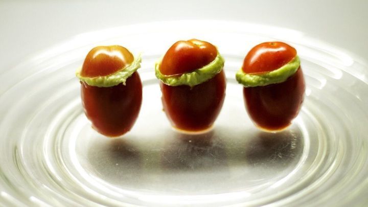 Mini-Tomaten stehen auf einem gl&auml;sernen Teller und sind mit cremigem Guacahummus gef&uuml;llt, serviert in ansprechender Anordnung.