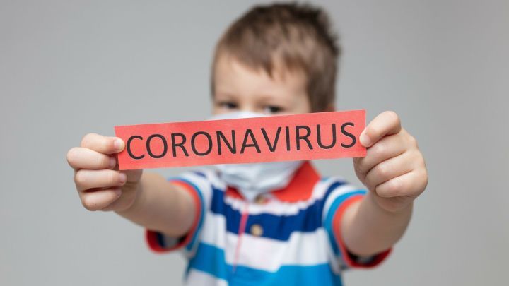 Ein Junge mit Mundschutz h&auml;lt ein rotes Schild mit der Aufschrift &bdquo;CORONAVIRUS&ldquo; in Richtung Kamera.