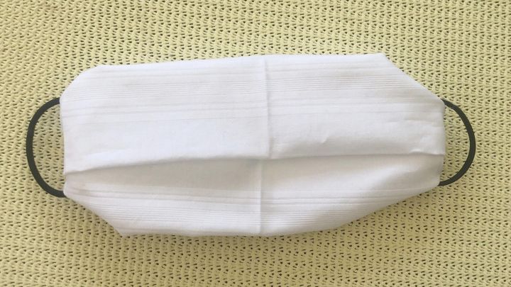 Eine wei&szlig;e Mund- und Nasenmaske liegt flach auf einem hellgr&uuml;nen Stoff, bereit zur Benutzung ohne N&auml;hen.