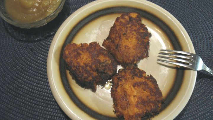 Drei goldbraun gebratene Kartoffel-K&uuml;chlein liegen auf einem Teller, begleitet von Apfelmus in einer Sch&uuml;ssel.