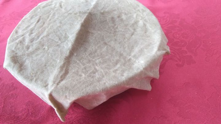 Ein Bienenwachstuch deckt eine runde Sch&uuml;ssel ab und sch&uuml;tzt so Lebensmittel auf einer pinken Unterlage.