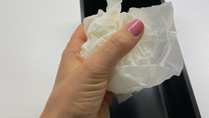 Eine Hand h&auml;lt zerkn&uuml;lltes Backpapier &uuml;ber einer schwarzen Backform, bereit, es einzulegen, um Fett zu ersetzen.