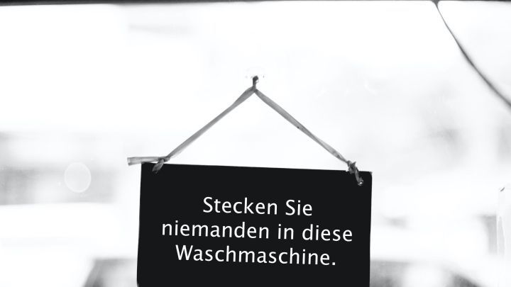 Ein schwarzes Schild h&auml;ngt an einer Waschmaschine und weist darauf hin: "Stecken Sie niemanden in diese Waschmaschine."