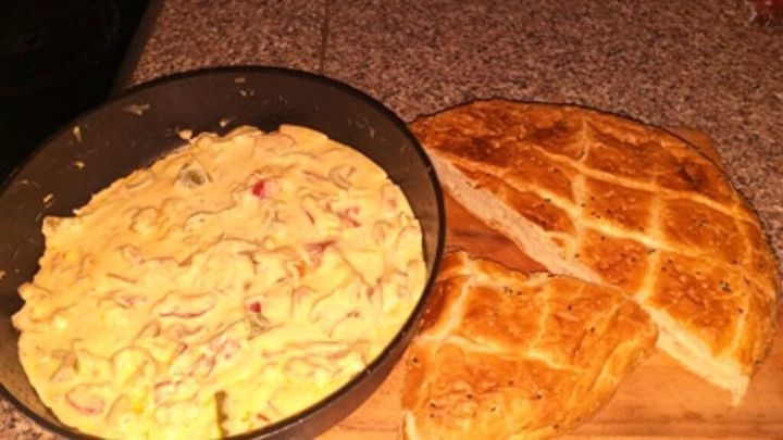 Eine Pfanne mit einer cremigen Paprika-Schmand-Mischung steht neben einem frisch gebackenem Brot auf einer K&uuml;chenoberfl&auml;che.