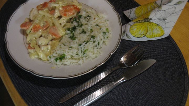 Ein Teller Rahmgeschnetzeltes mit Gem&uuml;se und Butterreis liegt auf einem Tisch, umgeben von Besteck und einer Serviette.