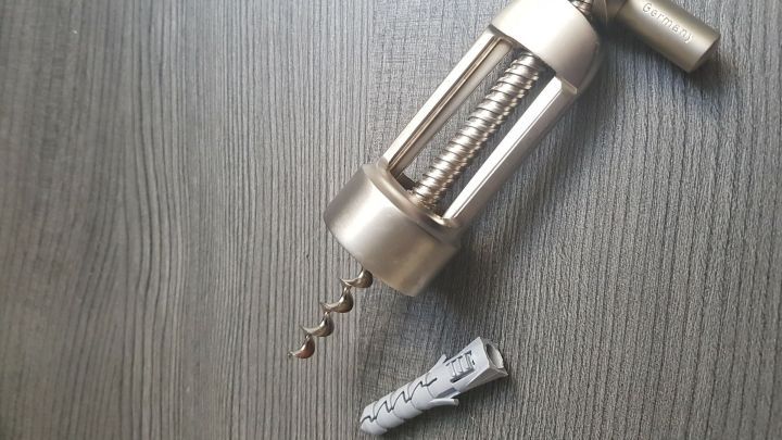 Ein gro&szlig;er, dicker D&uuml;bel wird mit einem speziellen Werkzeug von einer holzfarbenen Oberfl&auml;che entfernt.