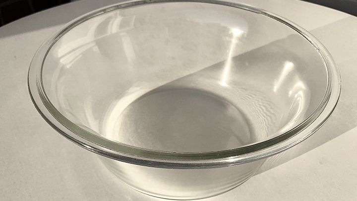 Ein rundes, durchsichtiges Glasfenster von einer Waschmaschine liegt auf einem Tisch und reflektiert das Sonnenlicht.