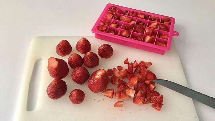 Erdbeeren werden auf einem Schneidebrett geschnitten und in eine pinke Gefrierebene gelegt, um sie portioniert einzufrieren.