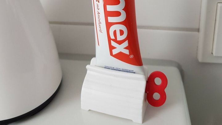 Eine Tube Zahnpasta steht in einem Tubenaufroller, der das Ausdr&uuml;cken erleichtert. Der Aufroller ist wei&szlig; mit einer roten Zahl 8.