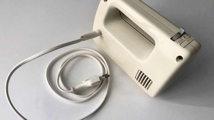 Ein Handmixer mit einem entworrenden Elektrokabel liegt auf einem wei&szlig;en Tisch, bereit zur Verwendung in der K&uuml;che.