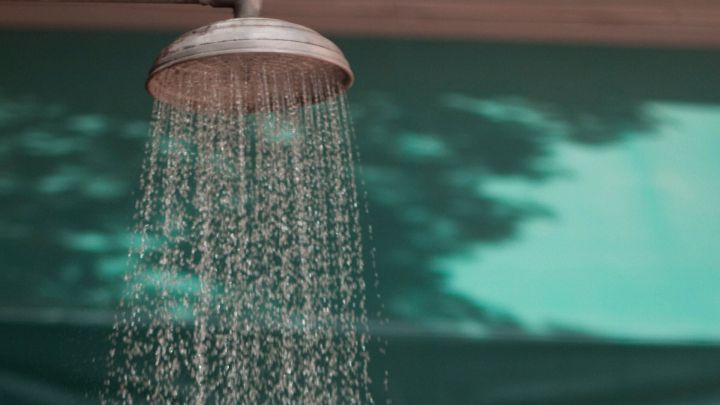 Eine Frau steht unter einer Dusche, w&auml;hrend kaltes Wasser auf sie herabstr&ouml;mt, um Muskelkater zu lindern.