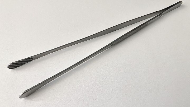 Eine Kochpinzette liegt auf einer wei&szlig;en Oberfl&auml;che, bereit f&uuml;r pr&auml;zises Anrichten und vielseitige Anwendungen in der K&uuml;che.