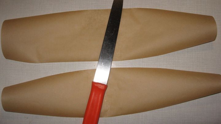 Zwei braune Papierstreifen liegen nebeneinander, w&auml;hrend ein K&uuml;chenmesser mit rotem Griff auf einer der Kanten aufliegt.