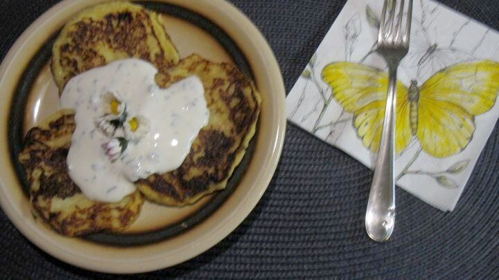 Kleine Kartoffel-Pfannenkuchen liegen auf einem Teller, garniert mit einer wei&szlig;en Sauce, neben einer Serviette mit Schmetterling.