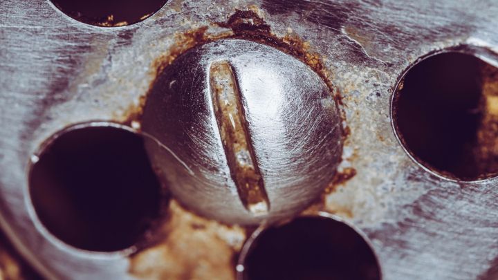 Eine verrostete Schraube sitzt fest in einer Metalloberfl&auml;che, w&auml;hrend Eisspray auf die Schraube gespr&uuml;ht wird, um sie zu l&ouml;sen.