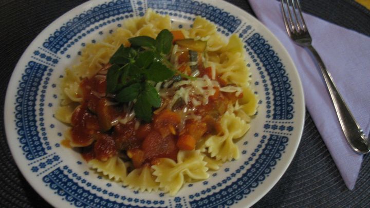 Ein Teller mit Farfalle-Pasta, belegt mit einer bunten Gem&uuml;se-Bolognese, garniert mit Kr&auml;utern und K&auml;se.