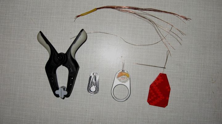 Eine N&auml;hnadel-Einf&auml;delhilfe liegt auf einem hellen Untergrund, umgeben von verschiedenen kleinen Werkzeugen.