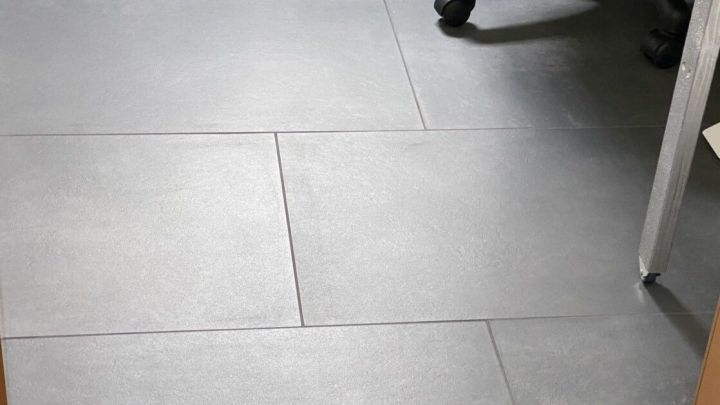 Ein dunkler Fliesenboden wird gepflegt, w&auml;hrend ein Stuhl im Hintergrund steht, was eine saubere Umgebung andeutet.