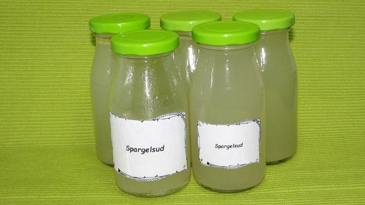 F&uuml;nf Gl&auml;ser Spargelsud stehen auf einem gr&uuml;nen Hintergrund, bereit zur Verwendung in einer Gem&uuml;sezubereitung.