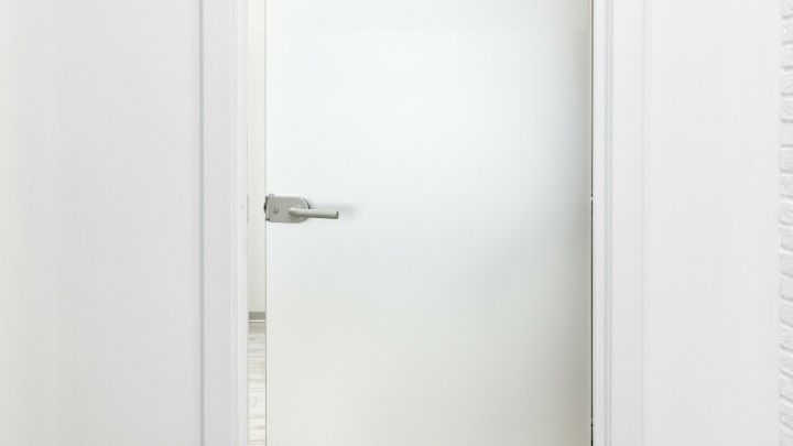 Eine satinierte Glast&uuml;r steht offen, w&auml;hrend Klebereste an der Glasoberfl&auml;che sichtbar sind, in einem hellen Raum.