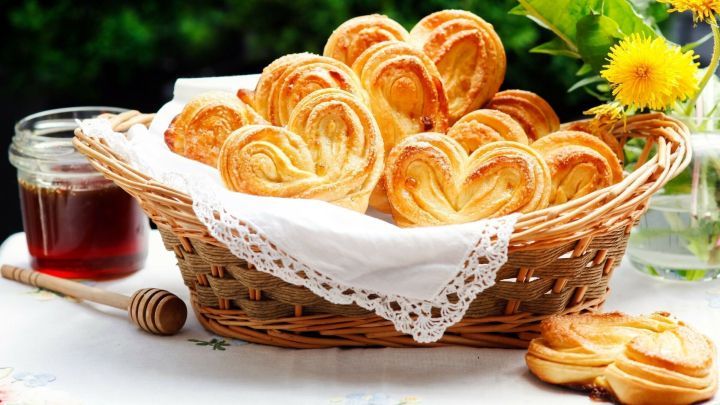 Frisch gebackene Pluschki-Hefeteilchen liegen in einem Korb, umgeben von Blumen und einem Glas Honig.