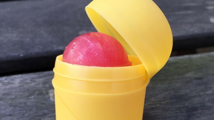 Eine gelbe &Uuml;-Ei-Verpackung, die ge&ouml;ffnet ist und einen roten Lolli zeigt, steht auf einem Holztisch im Freien.