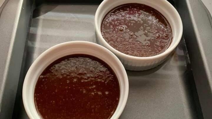 Zwei Schalen mit fl&uuml;ssigem Schokoladenteig stehen in einer Backform auf einer K&uuml;chenoberfl&auml;che, bereit f&uuml;rs Backen.