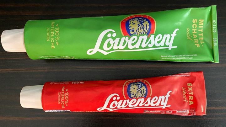 Zwei Senftuben stehen nebeneinander auf einem dunklen Holztisch, bereit f&uuml;r leckere So&szlig;en f&uuml;r verschiedene Gerichte.