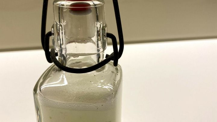 Ein kleines Glasfl&auml;schchen steht auf einem wei&szlig;en Tisch. Es enth&auml;lt transparentes Aloe Vera-Gel und ist verschlossen.